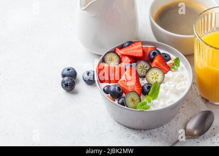 Cottage cheese with strawberries, nuts and blueberries in a gray bowl for breakfast. Summer recipe. Stock Photo