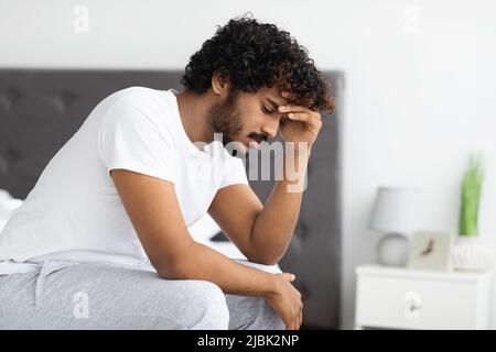 Depressed indian guy sitting on bed at home Stock Photo