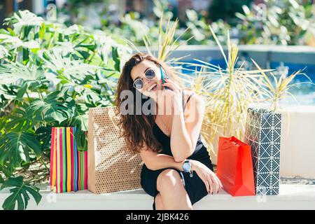 A young beautiful woman calls a taxi to the mall, talks on the phone, talks about the purchases she made in the mall, enjoys shopping and new clothes. Stock Photo
