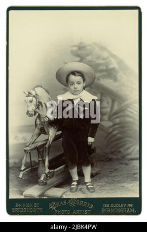 Original charming Victorian era Cabinet card of a cute young boy wearing a velvet suit with a lace collar (Little Lord Fauntleroy style) standing next to a beautiful rocking horse.  From the studio of Chas (Charles) Norris, with studios at  High St. Bridgnorth, Shropshire and Dudley Rd, Birmingham, U.K. Circa late 1890's, 1900.
