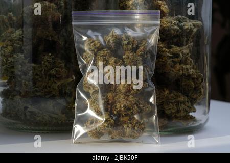 Dry and trimmed cannabis buds stored in a plastic bag on glass jars background with buds. Medical marijuana Stock Photo