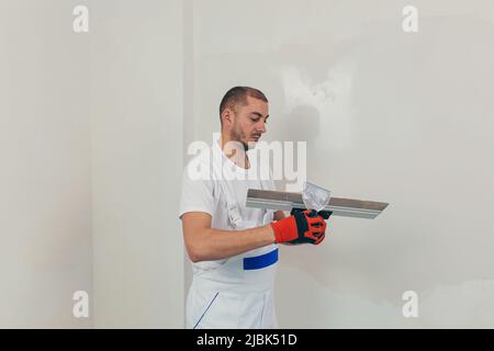 A man worker plasters the wall with a spatula and applies a cement mix solution. The repairman lays the plaster on the drywall Stock Photo