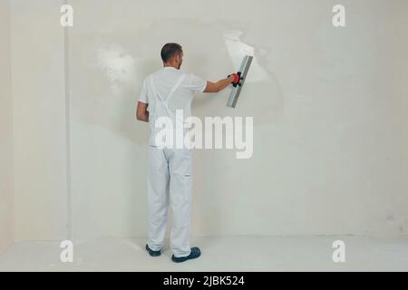 A man worker plasters the wall with a spatula and applies a cement mix solution. The repairman lays the plaster on the drywall Stock Photo