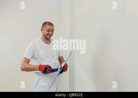 A man worker plasters the wall with a spatula and applies a cement mix solution. The repairman lays the plaster on the drywall Stock Photo
