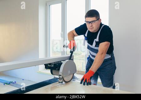 Master man, builder cuts a tile. Machine with a circular saw Stock Photo