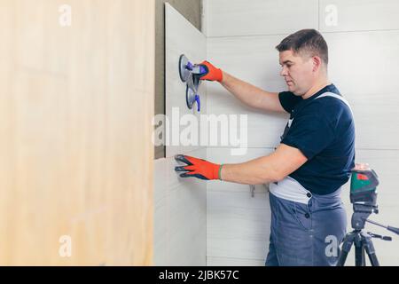A male construction worker installs a large ceramic tile Stock Photo