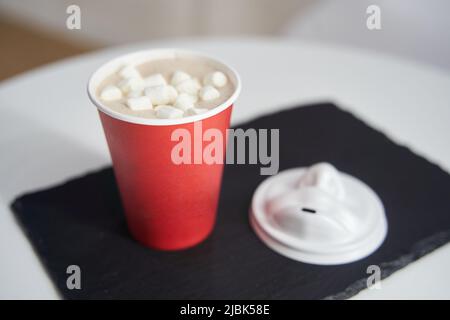 Red paper cup of coffee with marshmallows on a black tray. Stock Photo