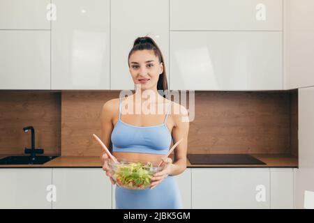 Young beautiful female nutritionist showing ready fresh vegetable salad, looking at camera, smiling Stock Photo