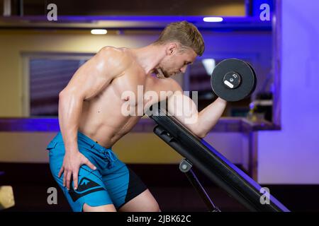 young handsome athletic man doing exercises in gym with dumbbells, looking at camera Stock Photo