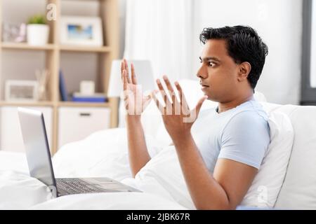 stressed indian man with laptop in bed at home Stock Photo