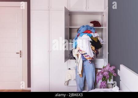 a woman holds a lot of crumpled clothes in her hands. Background room, large white closet. Stock Photo