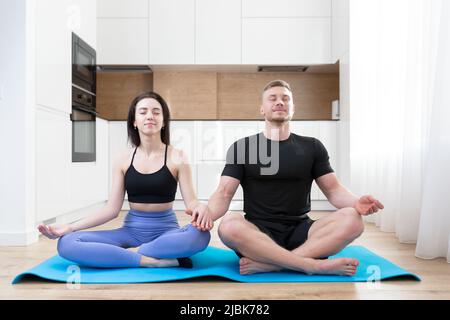 Young couple, man and woman doing yoga together at home on the mat Stock Photo