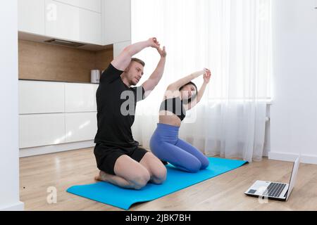 Young couple, man and woman play sports online from laptop at home on the rug, study, teach, train, exercise Stock Photo
