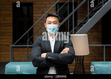 Portrait of a handsome, young Chinese Asian professional businessman in a suit wearing a protective medical mask on his face Stock Photo