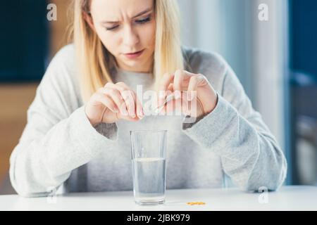 Beautiful young sick woman takes medication, puts pills in a glass of water for pain, sitting at the table Stock Photo