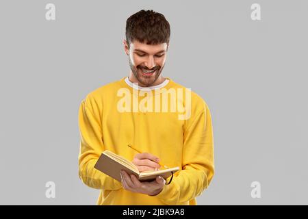 smiling man in yellow sweatshirt writing to diary Stock Photo