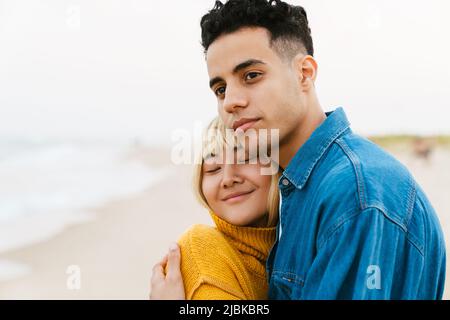 Multiracial young couple hugging while walking on beach Stock Photo