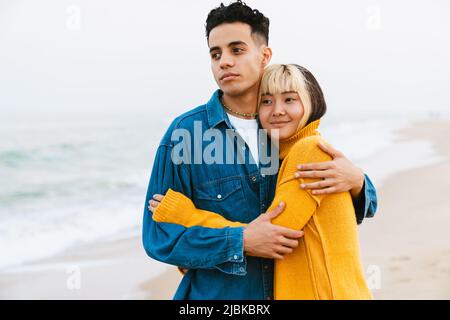 Multiracial young couple hugging while walking on beach Stock Photo