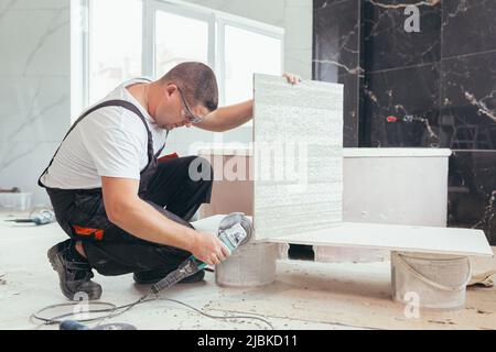 male worker cuts a large ceramic tile with an electric saw with a hand tool Stock Photo