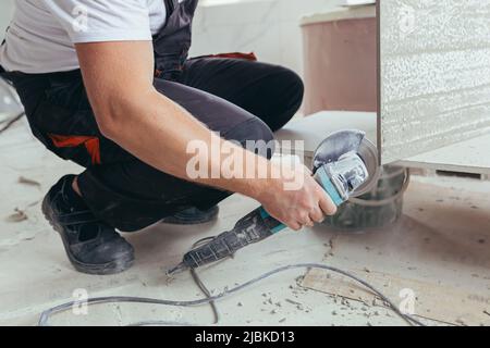 male worker cuts a large ceramic tile with an electric saw with a hand tool Stock Photo