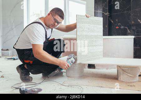male worker cuts a large ceramic tile with an electric saw with a hand tool Stock Photo