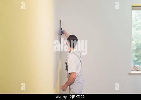 A working man applies putty to the walls in the apartment with a spatula, makes repairs in a new house Stock Photo