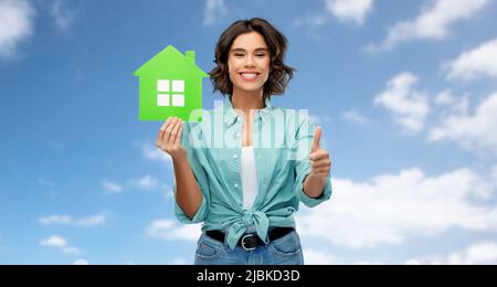 smiling woman with green house showing thumbs up Stock Photo