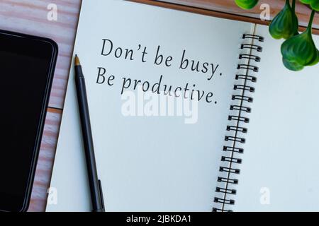 Motivational and inspirational quote on note book on wooden desk - Don't be busy, be productive. Stock Photo