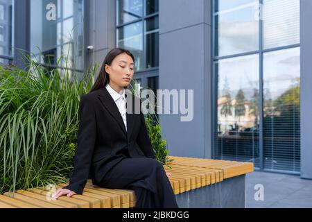 Sad asian fired woman sitting on bench depressed near office Stock Photo