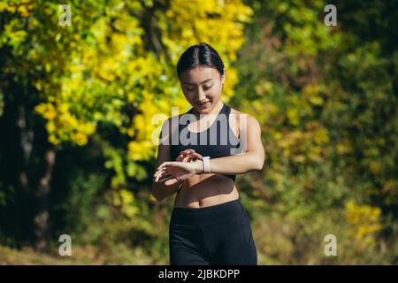 Portrait of young fitness woman athlete, asian looking at camera and smiling, enjoying fitness smart watch, for fitness Stock Photo