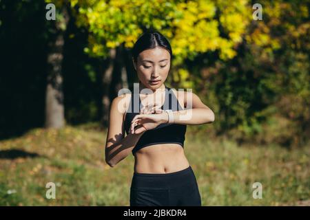 Sporty asian woman looking smart watch at modern track runner using use smartwatch fitness bracelet Portrait fitness female athlete checking result jo Stock Photo