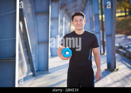 Active handsome male yogi walks in a stadium strolling before or after a workout. Young happy asian athletic man athlete goes to yoga class with a fit Stock Photo