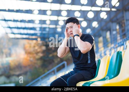 Tired male athlete resting, Asian holding his head, has a severe headache after running Stock Photo