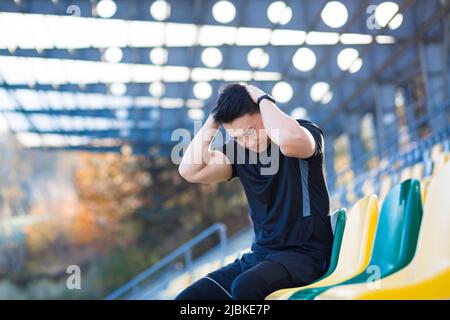 Tired male athlete resting, Asian holding his head, has a severe headache after running Stock Photo