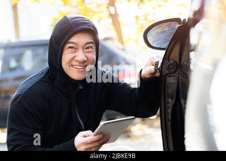 male bandit thief car thief asian uses a tablet to turn off the car alarm Stock Photo