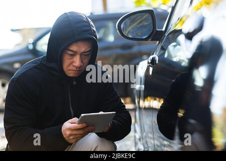 male bandit thief car thief asian uses a tablet to turn off the car alarm Stock Photo