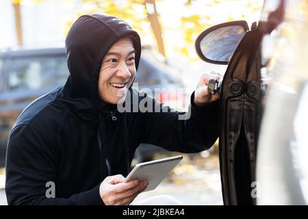 male bandit thief car thief asian uses a tablet to turn off the car alarm Stock Photo