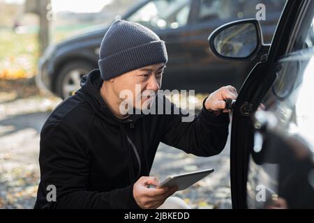 male bandit thief car thief asian uses a tablet to turn off the car alarm Stock Photo