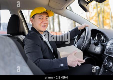 Male courier asian looks into the camera and smiles holding a parcel sitting in the car Stock Photo