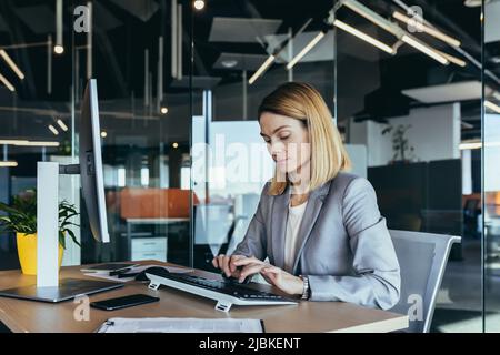 Portrait of a sensible and fair successful woman, businesswoman working in a modern office, at the computer, confident and focused Stock Photo