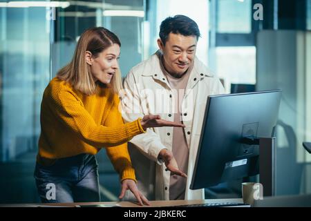 Employees of the IT company look at the computer monitor in surprise, an Asian man and a woman work in a modern office Stock Photo