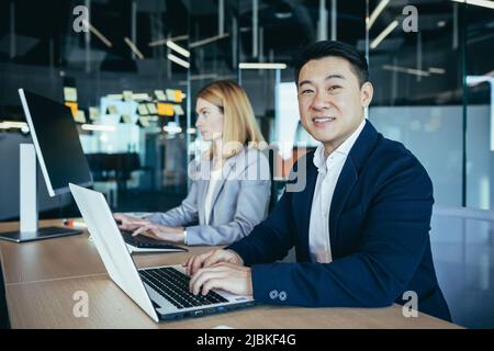 Asian businessman working in modern office on laptop, happy and successful, team of employees, man and business woman, startup Stock Photo