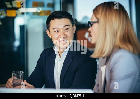Two employees are having fun. Asian man and blonde woman taking a break, colleagues working together in a modern office Stock Photo