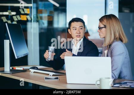 Two employees are having fun. Asian man and blonde woman taking a break, colleagues working together in a modern office Stock Photo