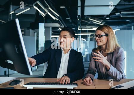 Happy and successful workers looking at computer monitor, Asian man and woman working in modern office Stock Photo