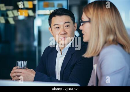 Two employees are having fun. Asian man and blonde woman taking a break, colleagues working together in a modern office Stock Photo