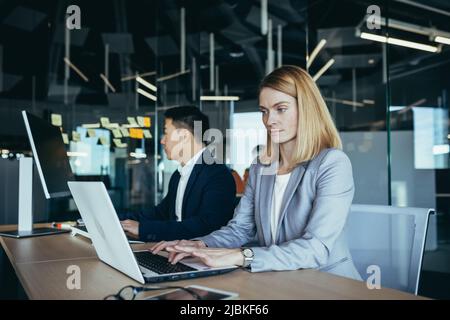 Blonde businesswoman working in modern office on laptop, team of business people working together Stock Photo