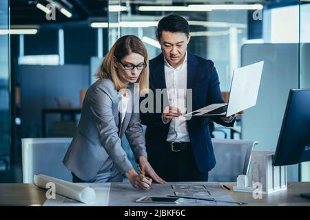A team of multiracial business architects and designers discuss creating a project draft drawing by looking at laptop monitor screen a computer desk. Stock Photo