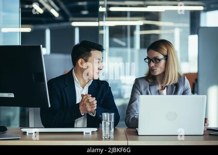 Friendly conversation of colleagues at work in the office. Asian man and Business woman communicate during work break. with a cup of coffee and a glas Stock Photo