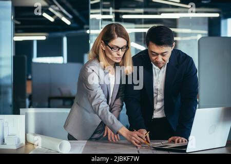 A team of multiracial business architects and designers discuss creating a project draft drawing by looking at laptop monitor screen a computer desk. Stock Photo